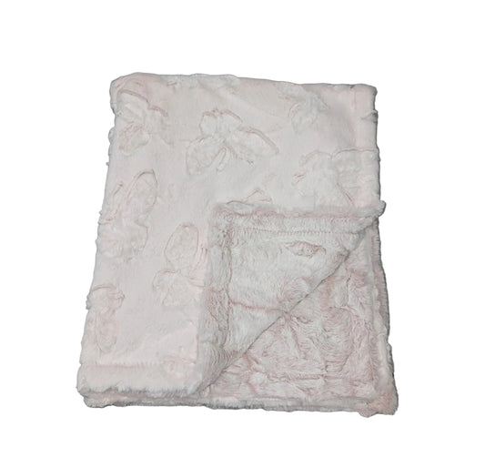 A folded light pink plush blanket with a subtle floral pattern, placed on a gray wood-plank floor.